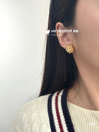 Gold-tone round stud earrings worn on ear with logo and clear rhinestones