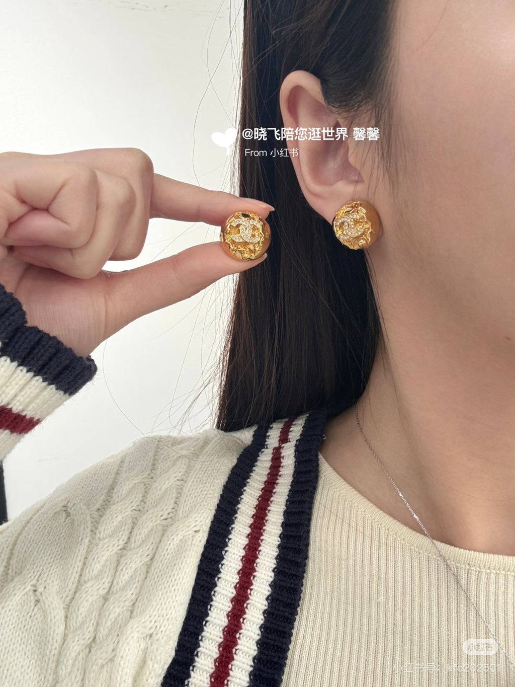 Gold-tone round stud earrings being adjusted on ear; logo and rhinestones visible