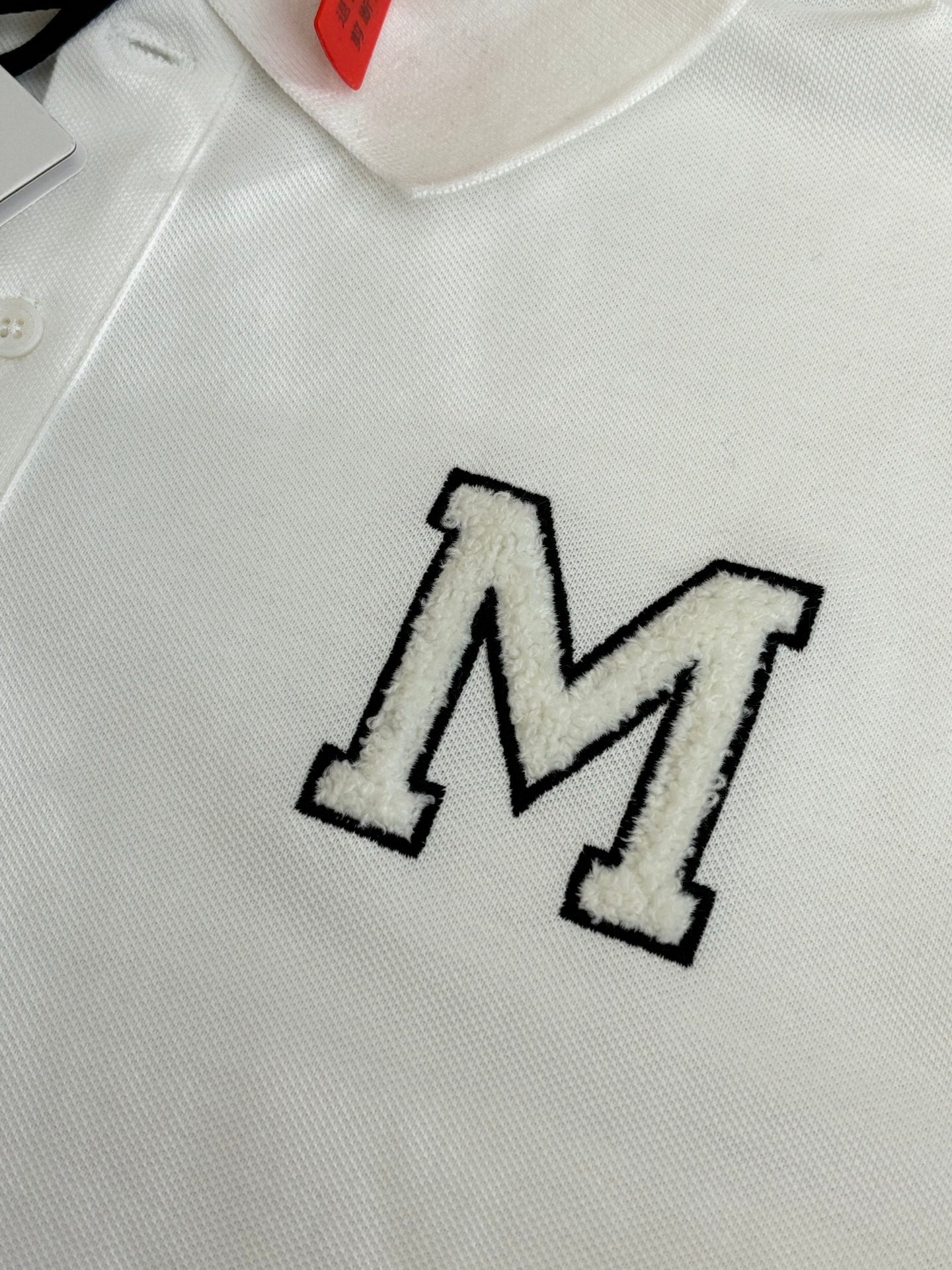 Close-up of white polo shirt with embroidered M logo on chest