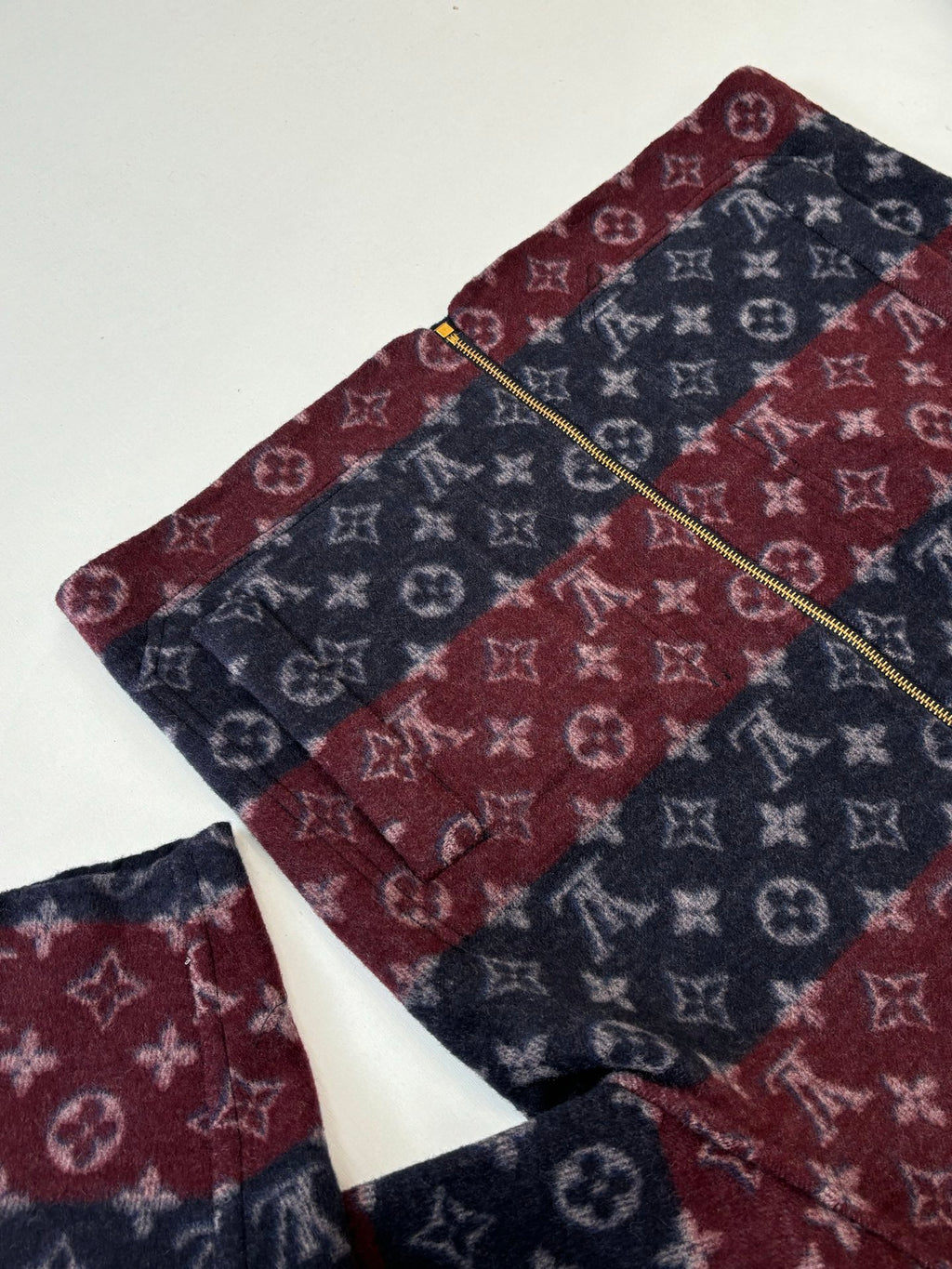 Maroon and navy monogram zip jacket with gold zipper line, collar visible.
