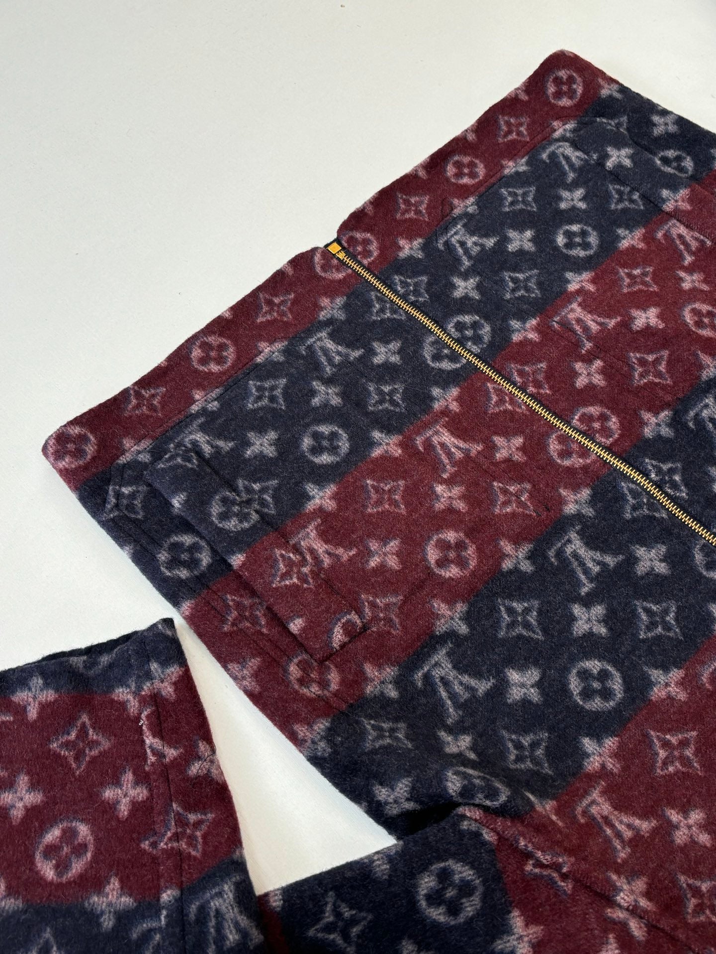 Maroon and navy monogram zip jacket with gold zipper line, collar visible.