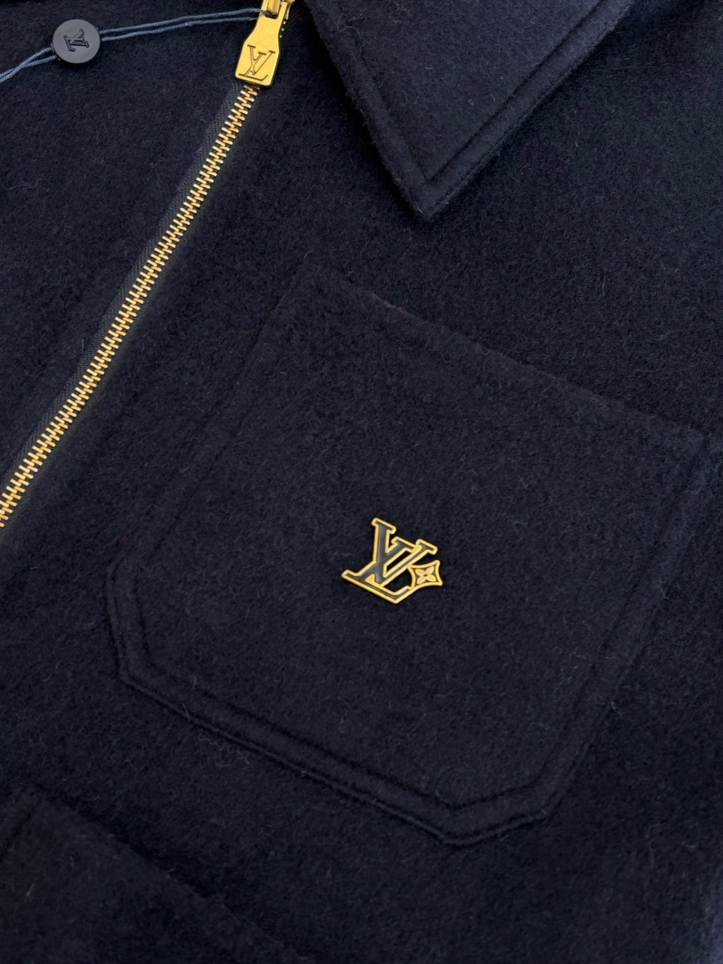 Dark navy Louis Vuitton jacket chest pocket with gold LV logo and gold zipper.