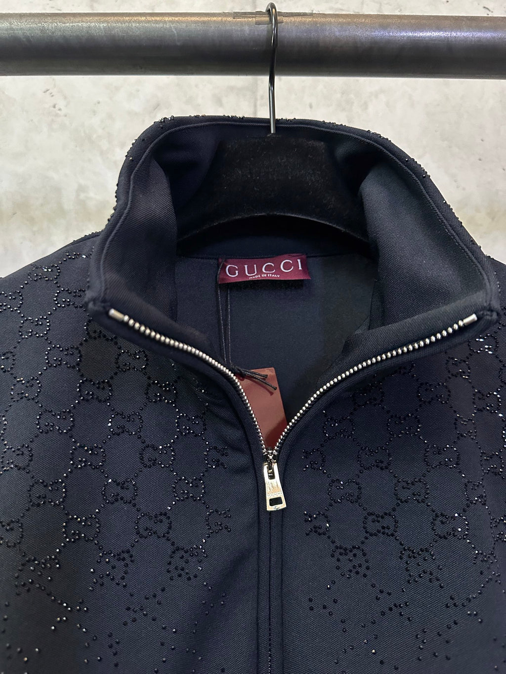 Dark Gucci monogram zip-up jacket showing Gucci label and metal zipper pull