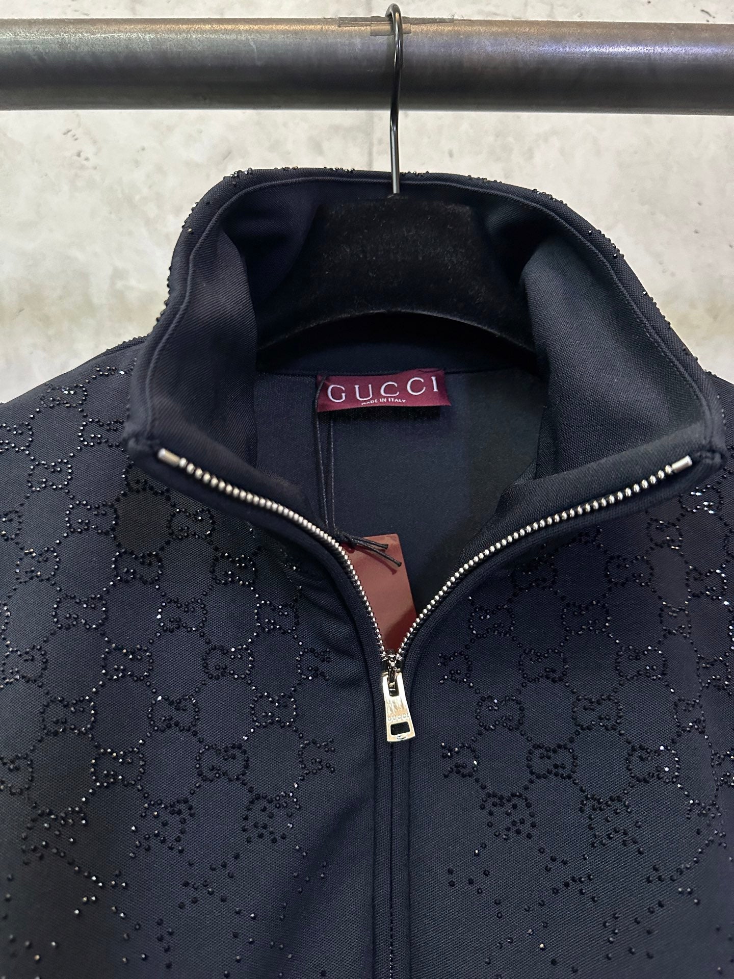 Dark Gucci monogram zip-up jacket showing Gucci label and metal zipper pull