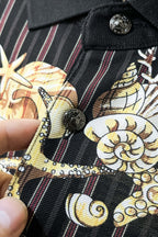 Black shirt fabric close-up with gold motif, red stripes, and button detail