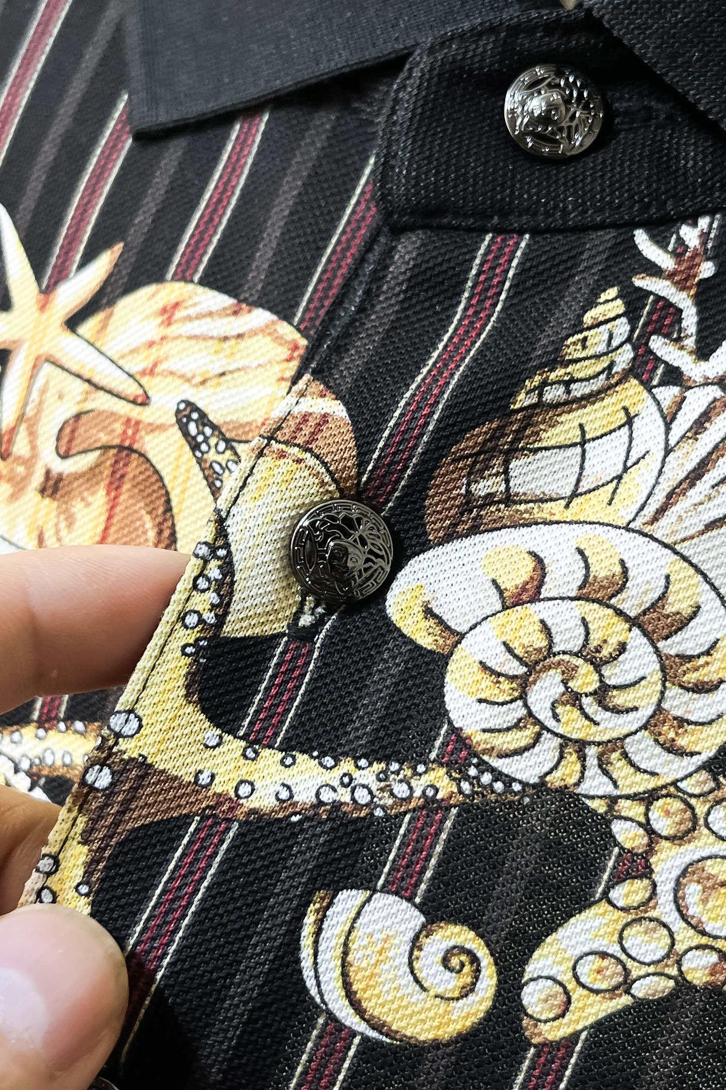 Black shirt fabric close-up with gold motif, red stripes, and button detail