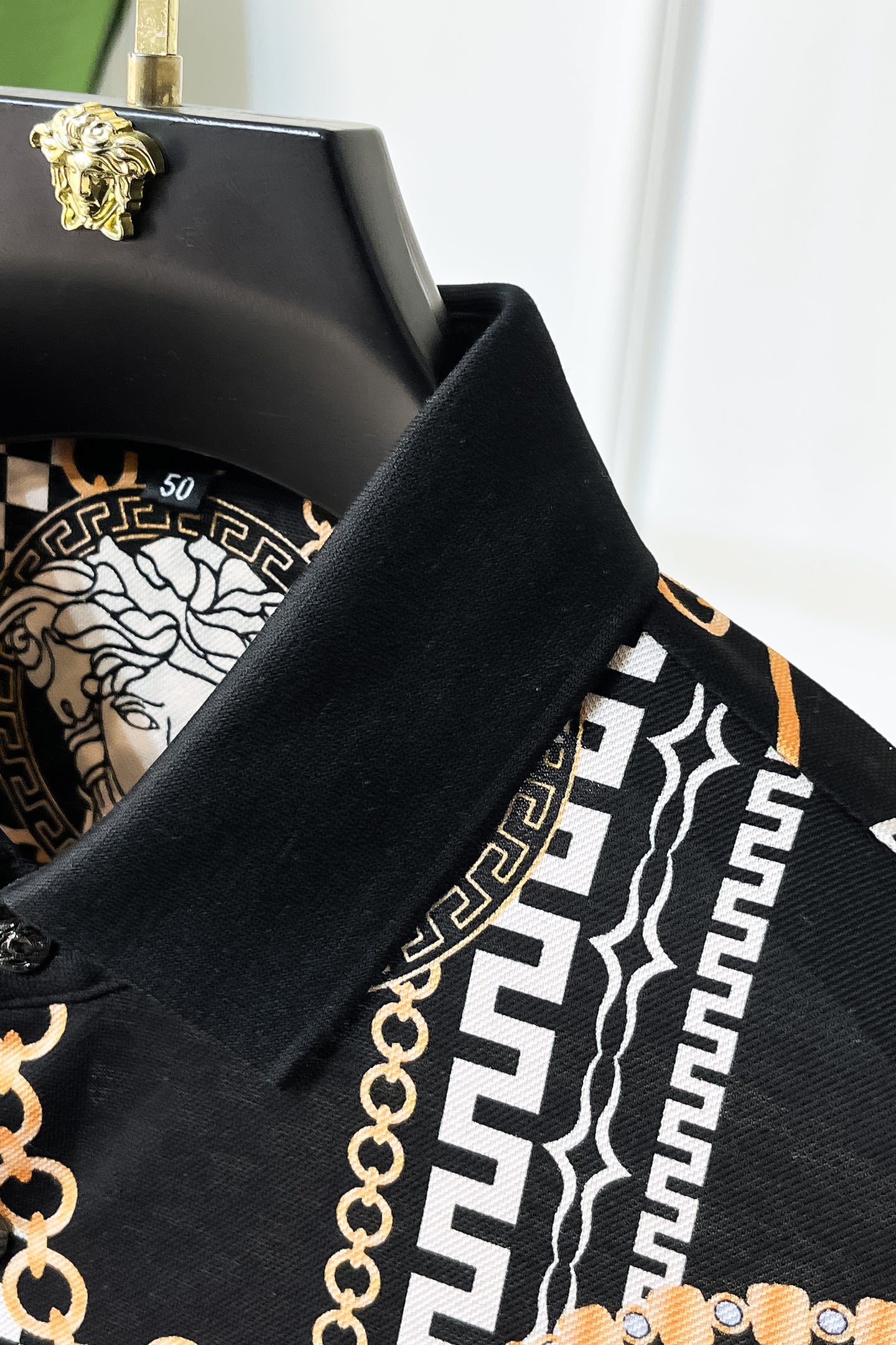 Versace shirt shoulder and collar detail with black fabric and gold-and-white Greek key pattern