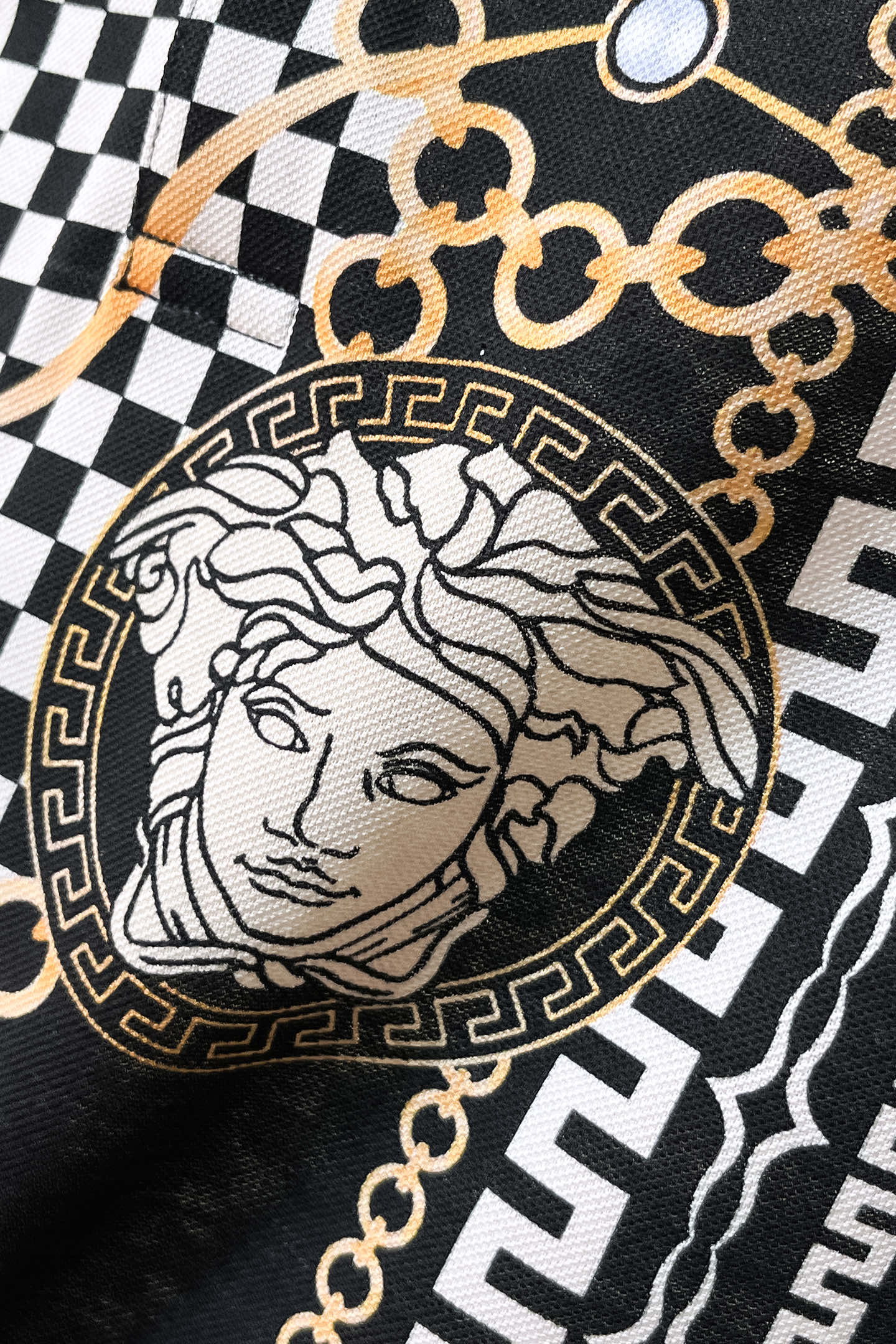 Versace fabric close-up: black-and-white checker print with Medusa bust emblem and gold trim