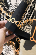 Versace sleeve cuff close-up with black collar trim and gold chain links on patterned fabric
