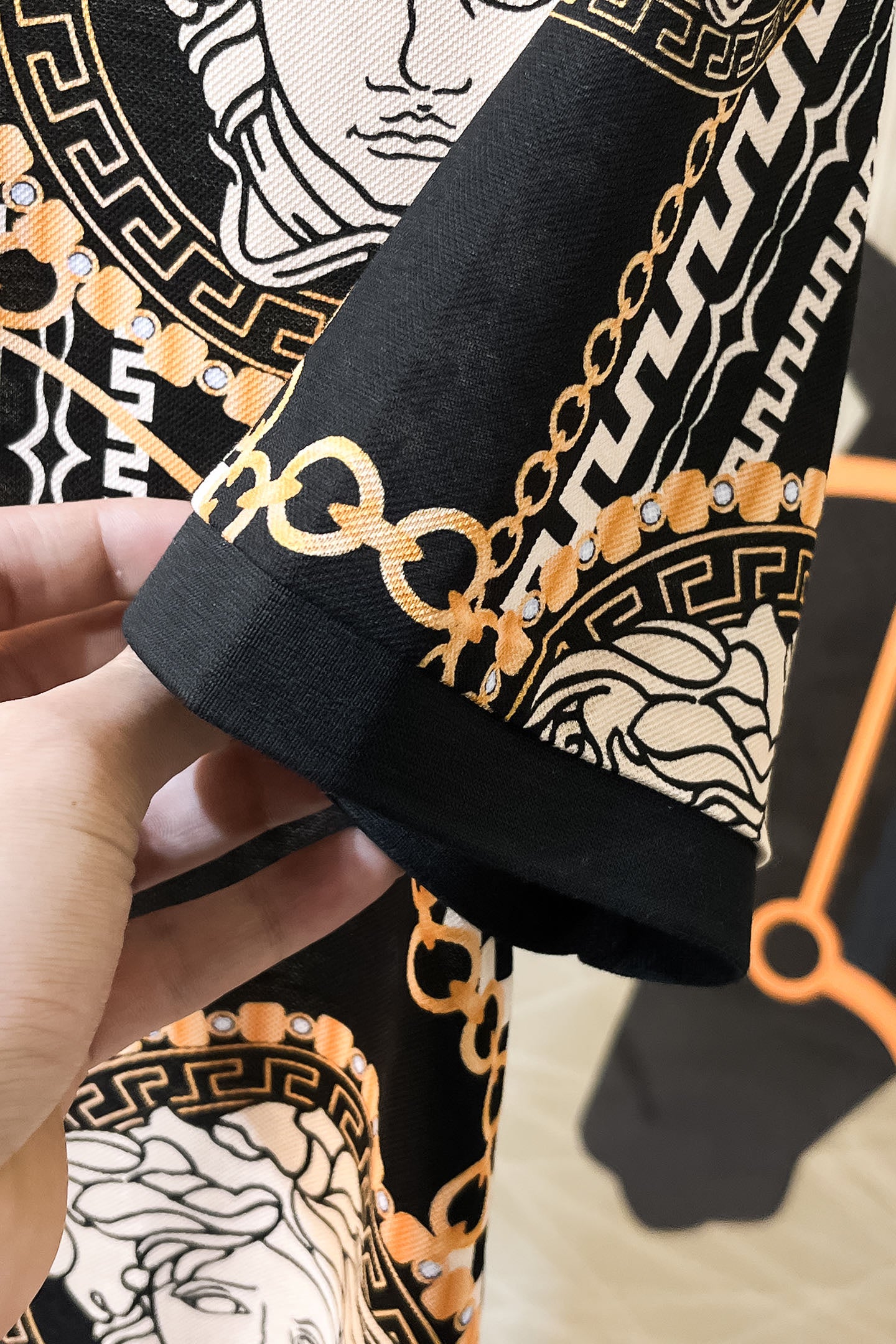 Versace sleeve cuff close-up with black collar trim and gold chain links on patterned fabric