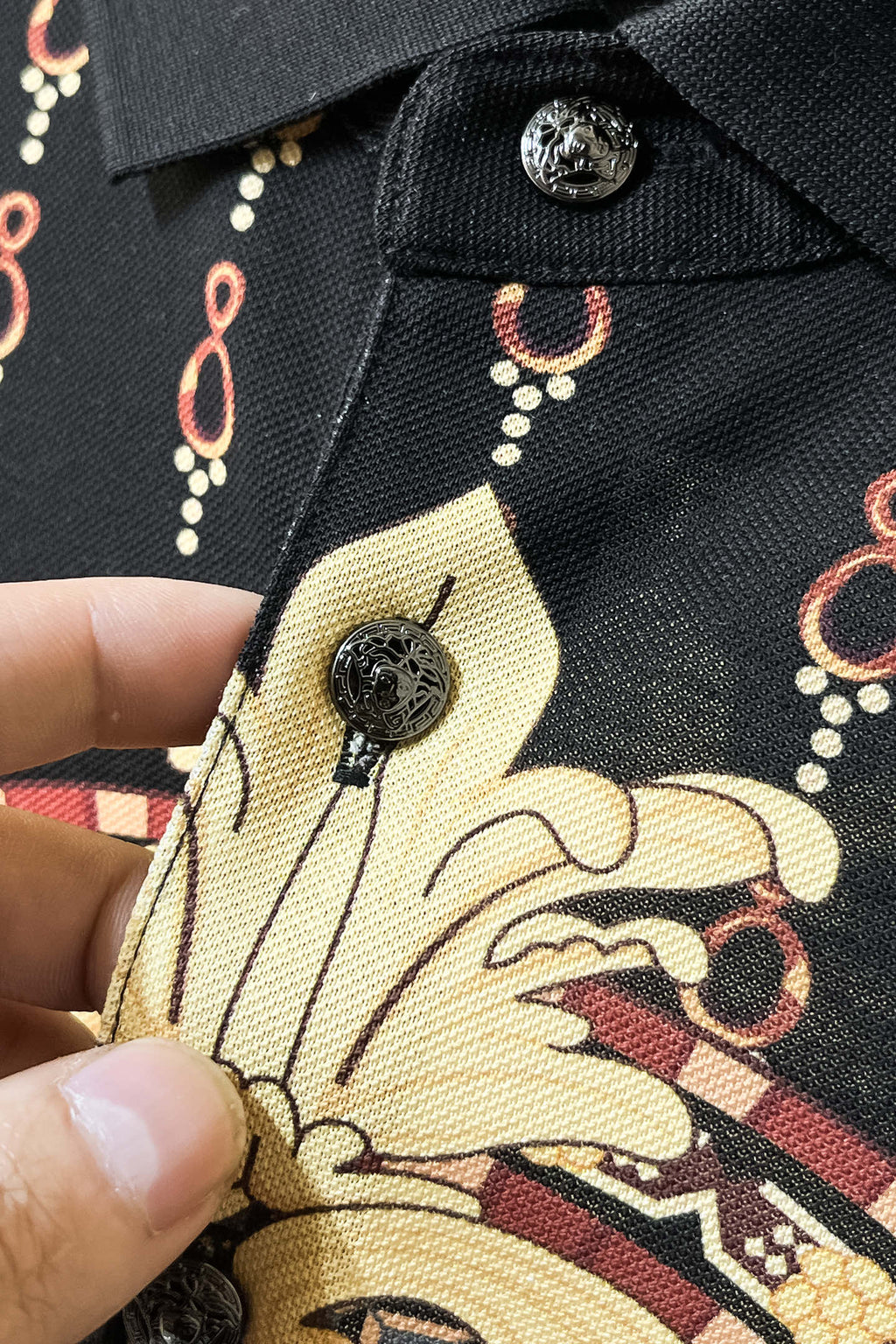 Black Versace polo collar close-up with button and red-gold chain trim
