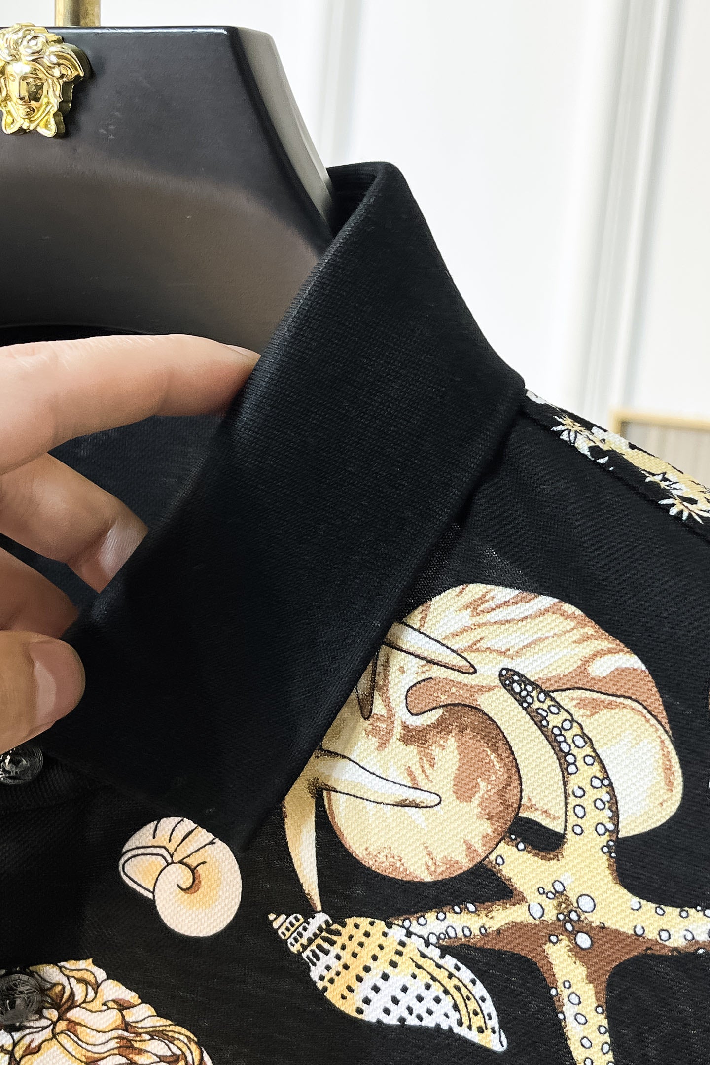 Versace polo shirt sleeve cuff detail with black fabric and gold, cream character print