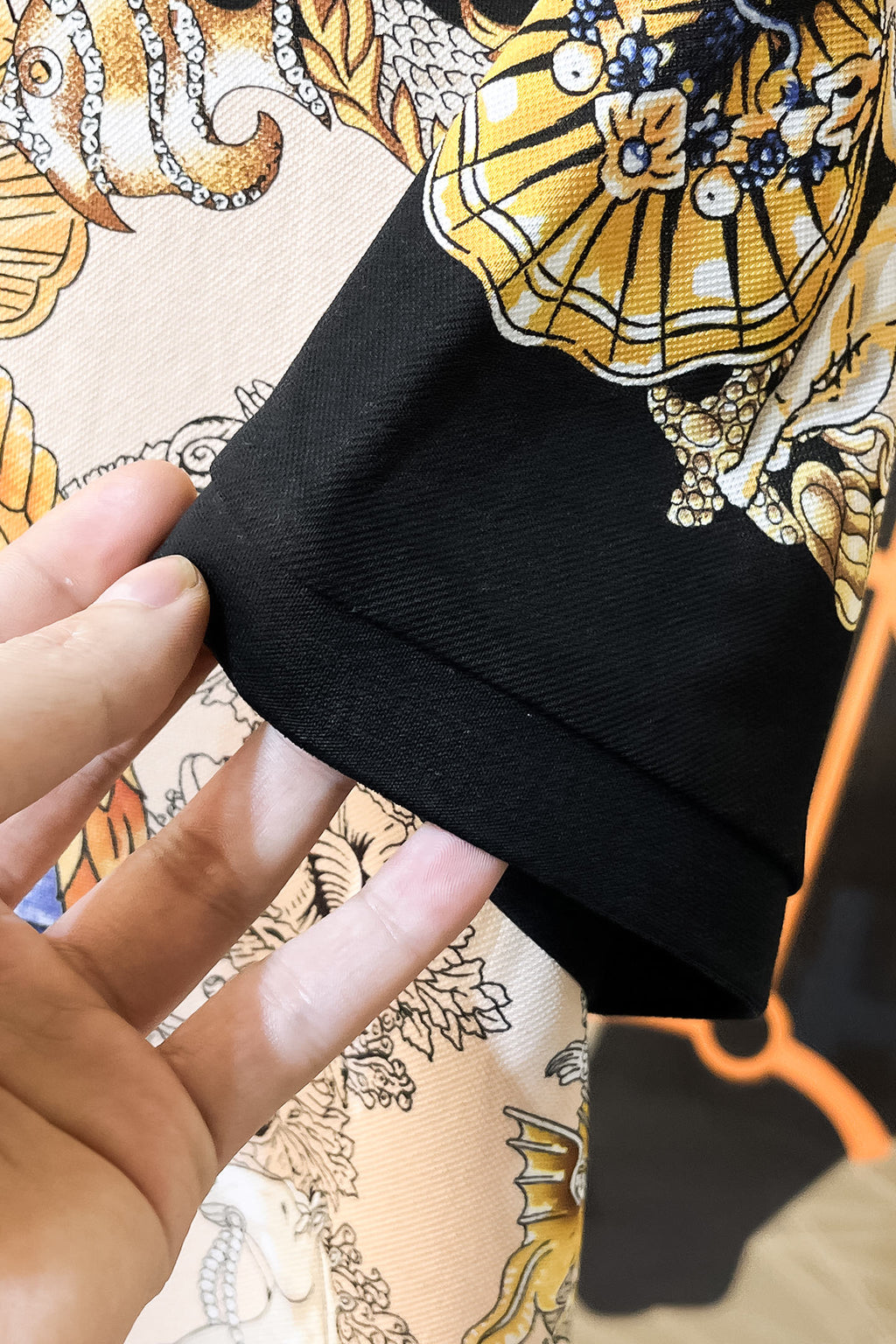 Versace polo shirt sleeve cuff close-up with black edging and gold, blue pattern