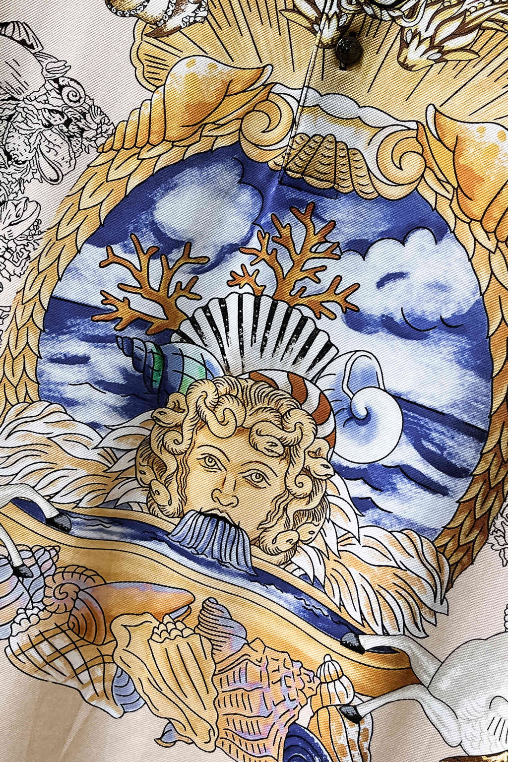 Versace polo shirt fabric detail with blue sky face and gold ornamental baroque lines