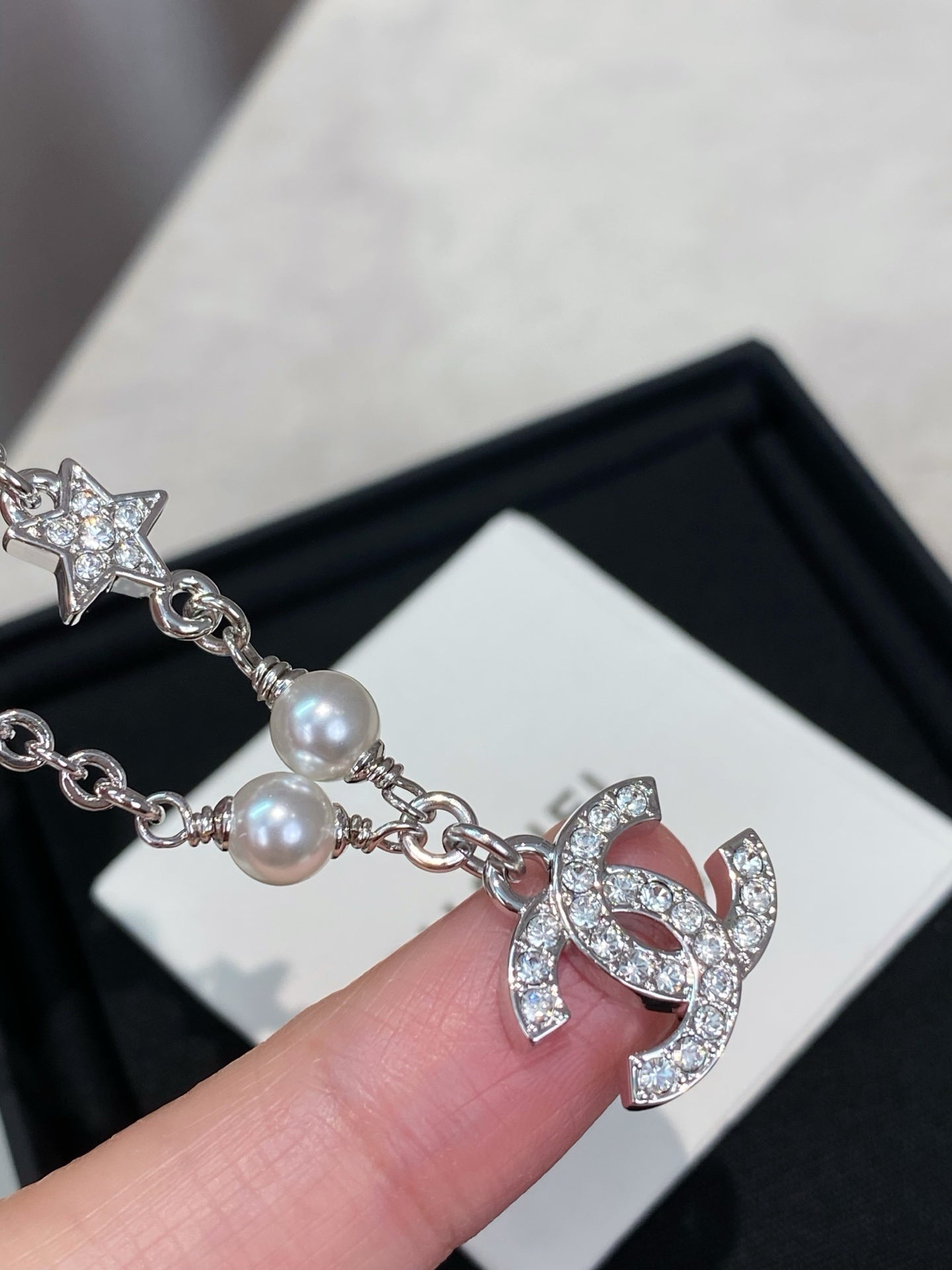 Close-up of silver charm bracelet with pearl bead and CC logo heart charm