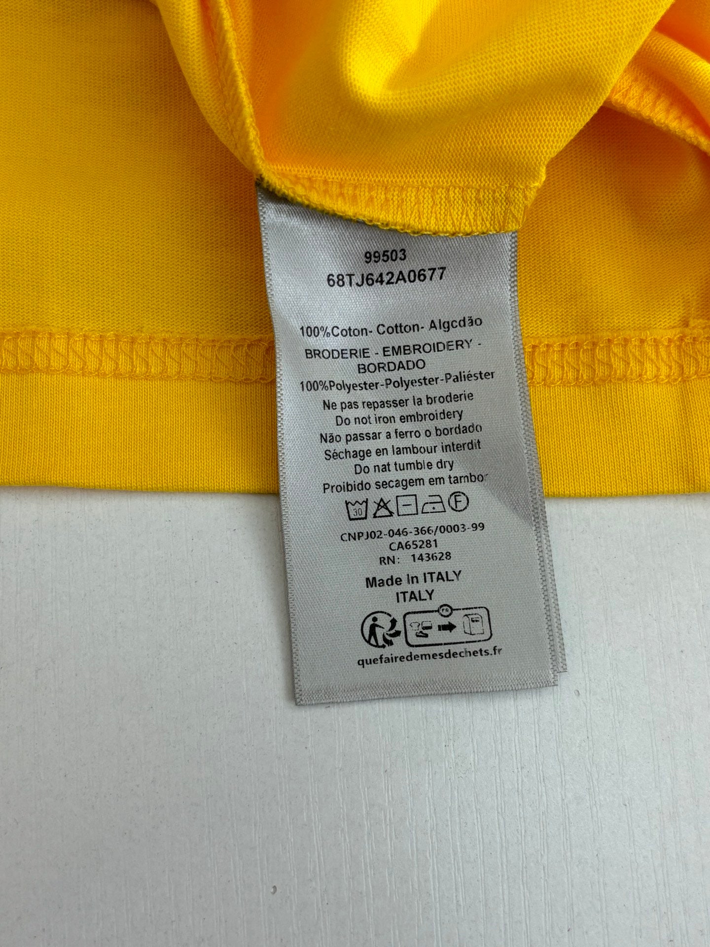 Yellow T-shirt care label with fabric and washing instructions.