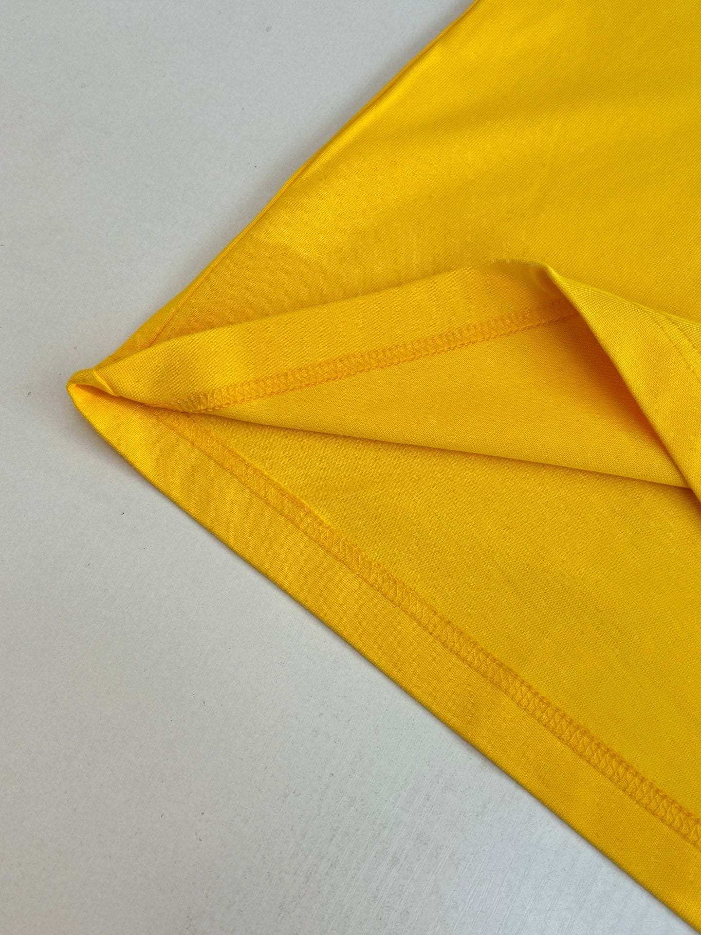 Folded yellow T-shirt showing stitched hem seam and smooth fabric texture.