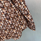 Long-sleeve button-up shirt with brown-and-cream monogram pattern, curved hem