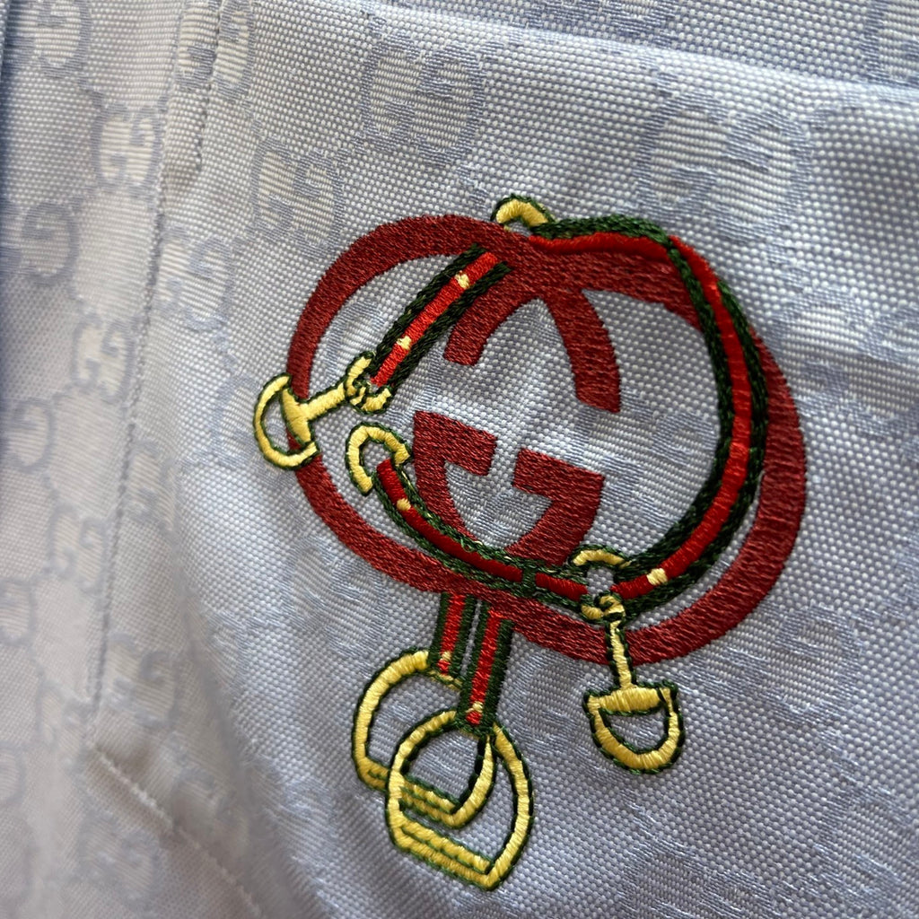 Embroidered crest patch on light blue Gucci shirt, red oval with multicolor accents