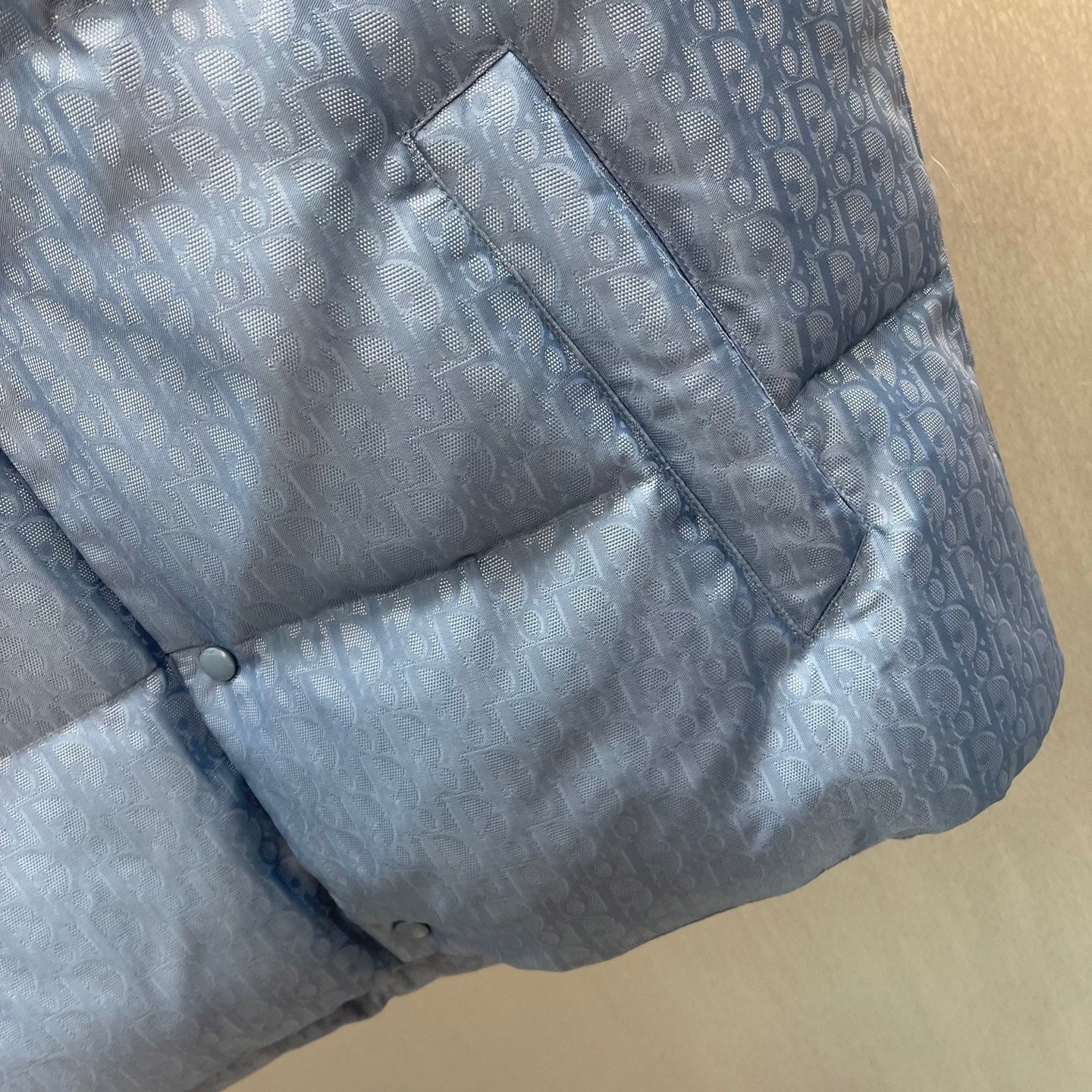 Light blue monogram puffer vest detail with seam stitching and button trim