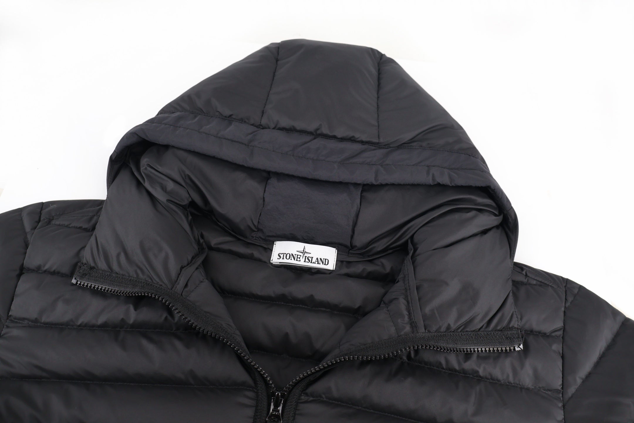 Stone Island puffer jacket hood close-up with chest logo label on black