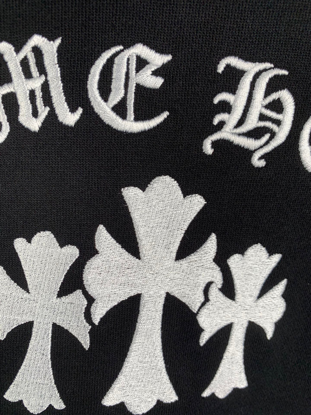 Black hoodie fabric with white cross-flower emblems and decorative lettering