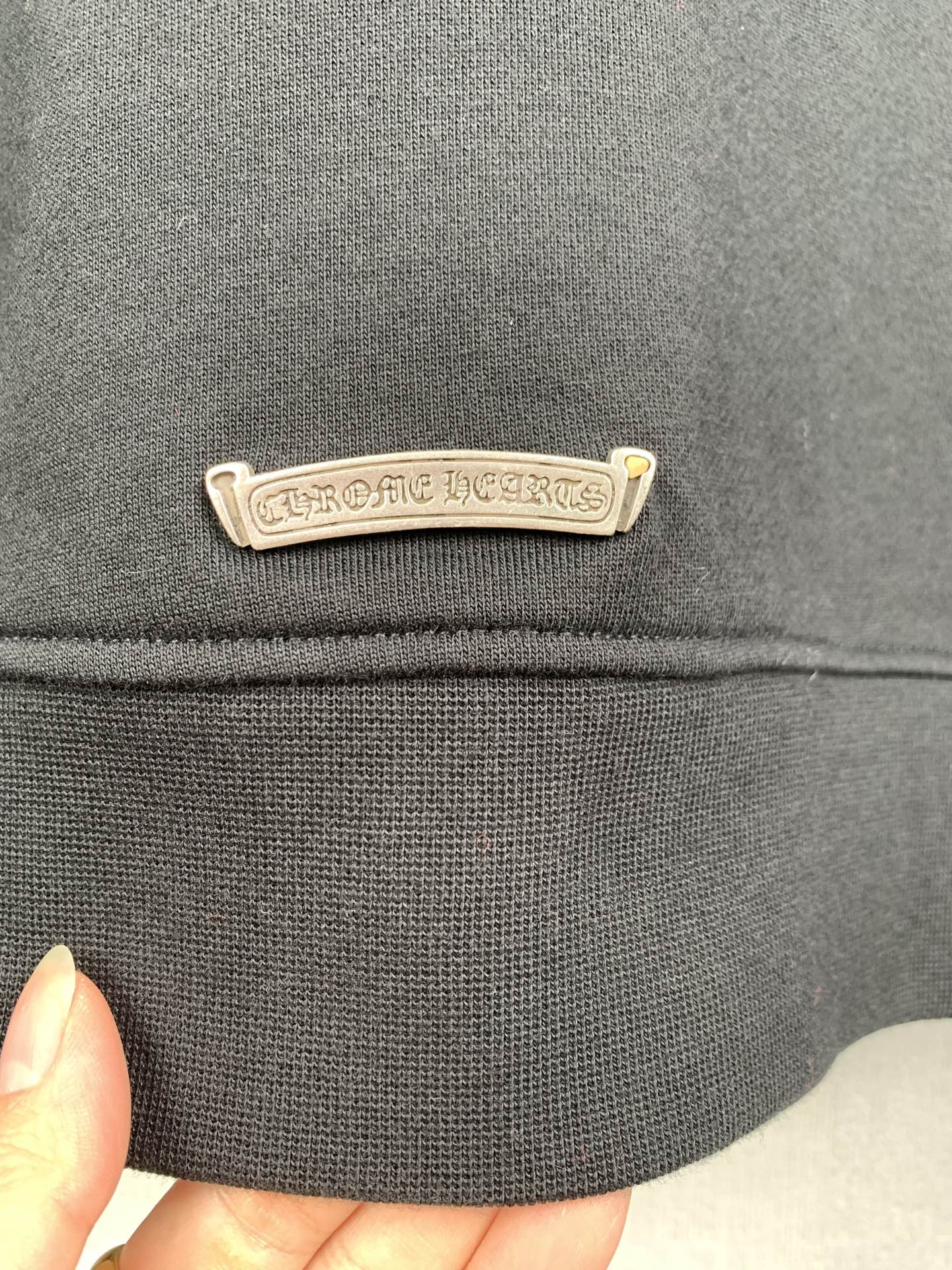 Dark gray hoodie chest logo label in chrome-tone metal