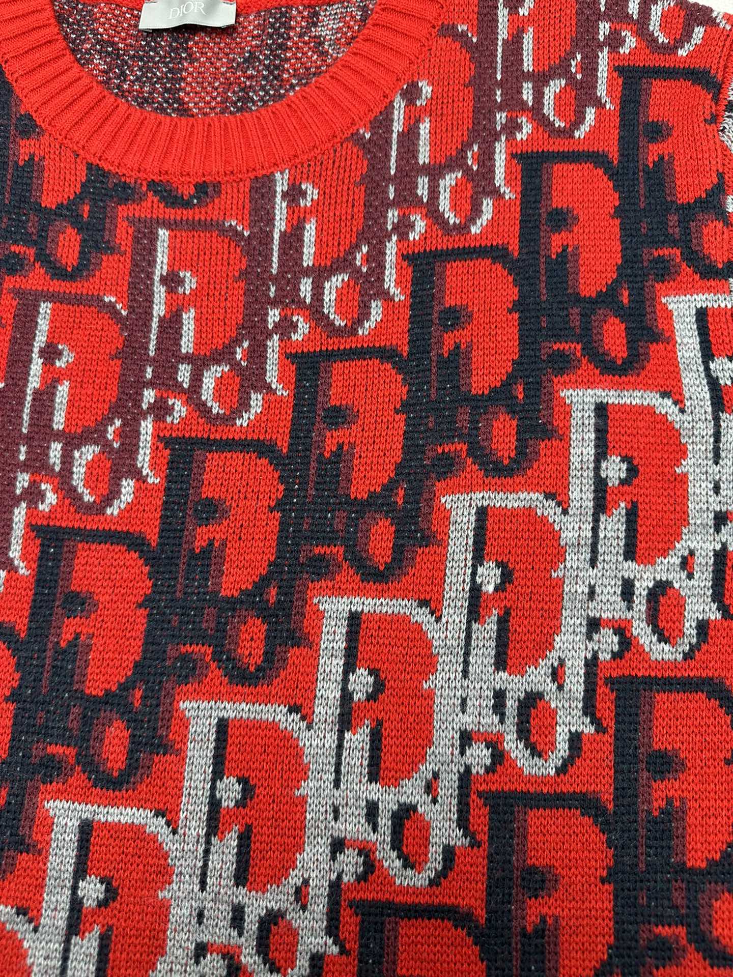 Dior knit sweater with red logo motif over dark blue knit, textured fabric surface
