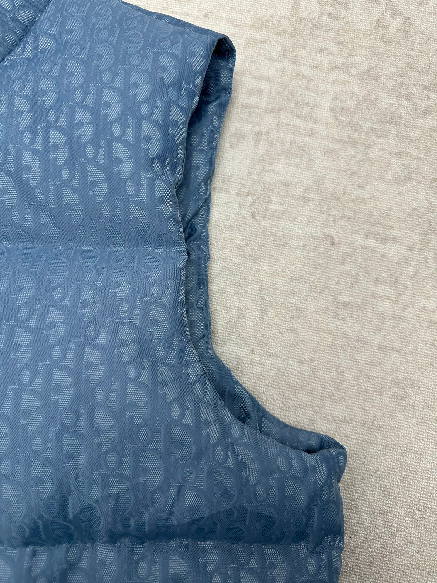 Blue Dior monogram puffer vest side view with curved hem and sleeveless armholes.