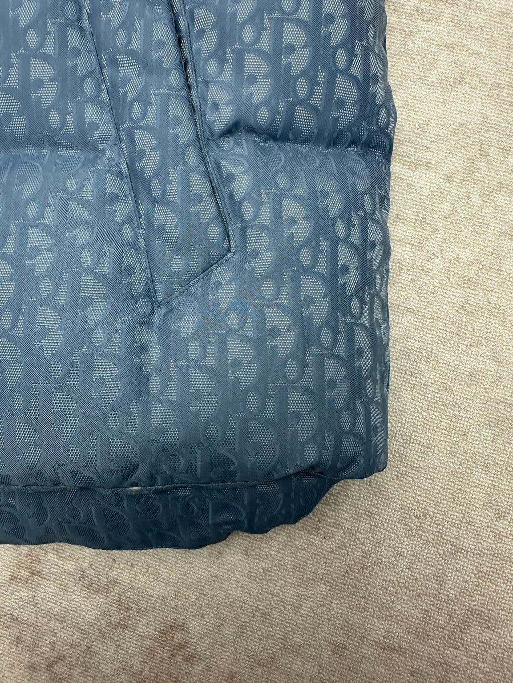 Blue Dior monogram puffer vest bottom hem detail with stitched quilting and curved edge.