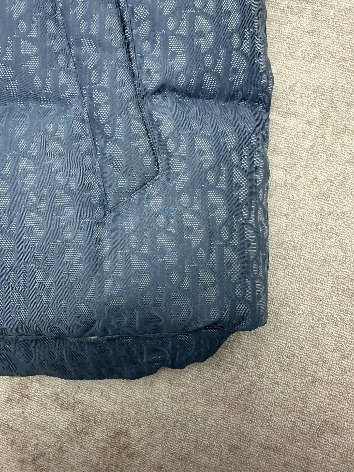 Blue Dior monogram puffer vest bottom hem detail with stitched quilting and curved edge.