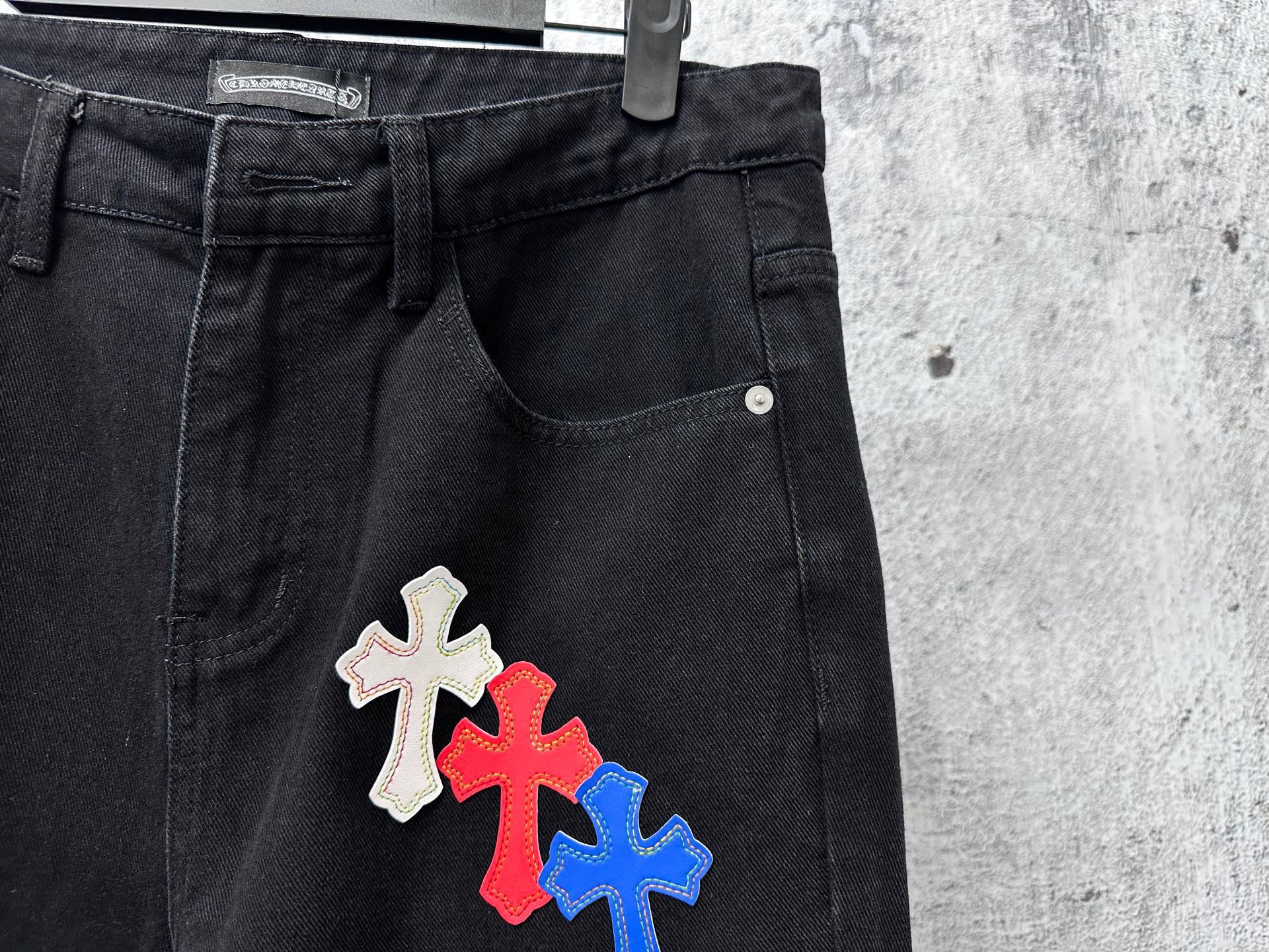 Black denim pants with multicolor cross patch near right pocket