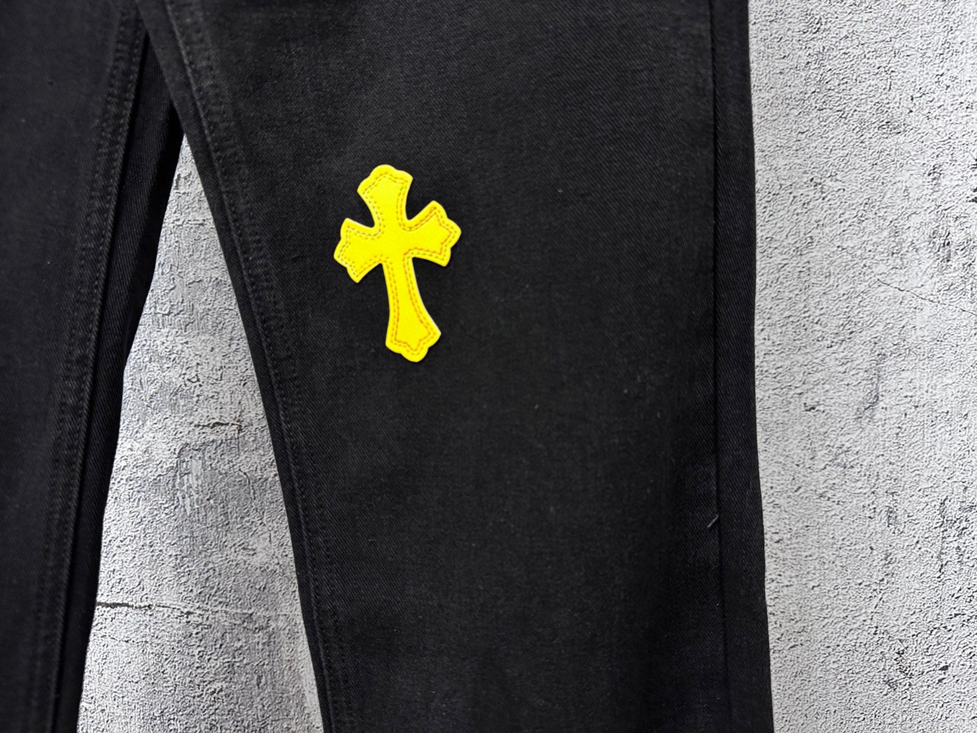 Black denim pants with yellow cross patch on upper thigh