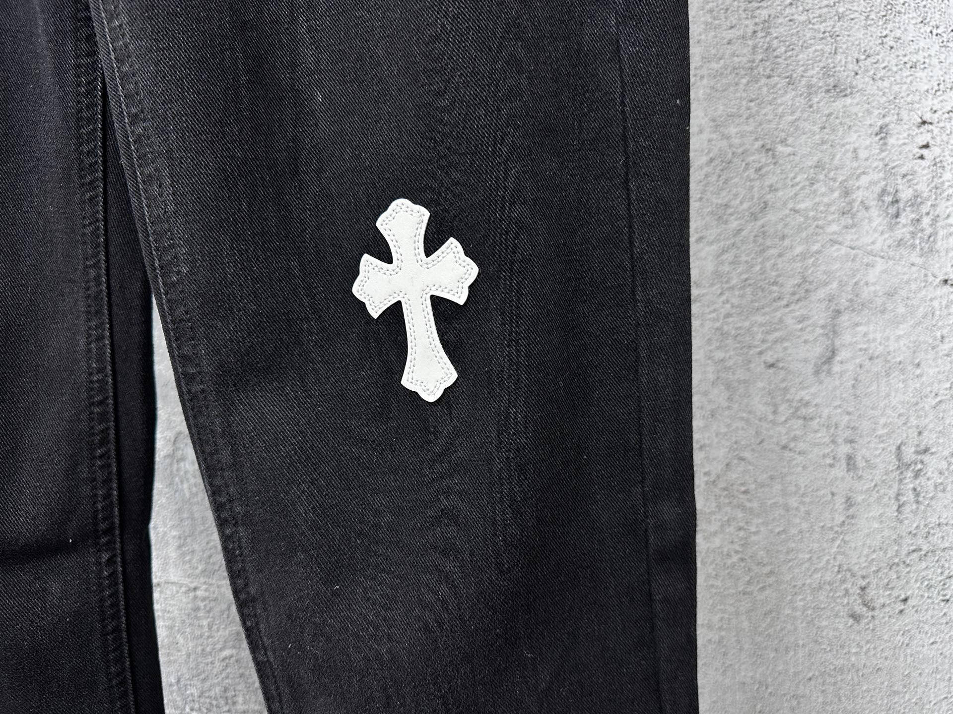 Dark denim pants with small white cross patch on thigh