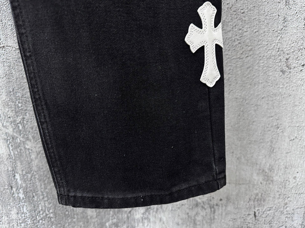 Dark denim pants hem with small white cross patch near lower leg