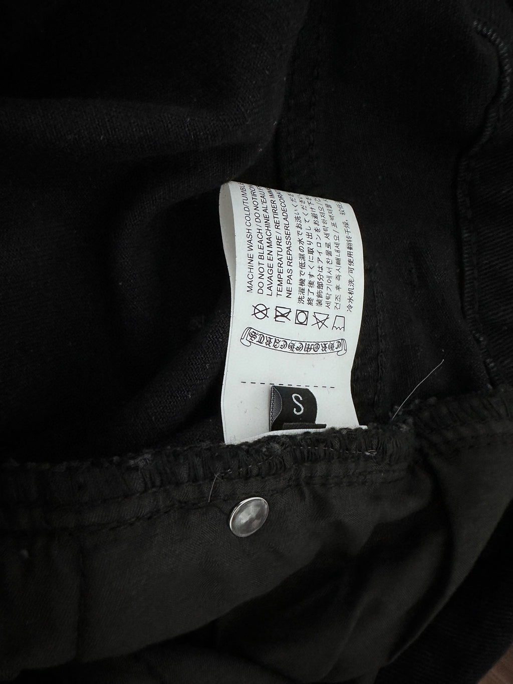 Dark denim pants inner waistband label with size S and care symbols