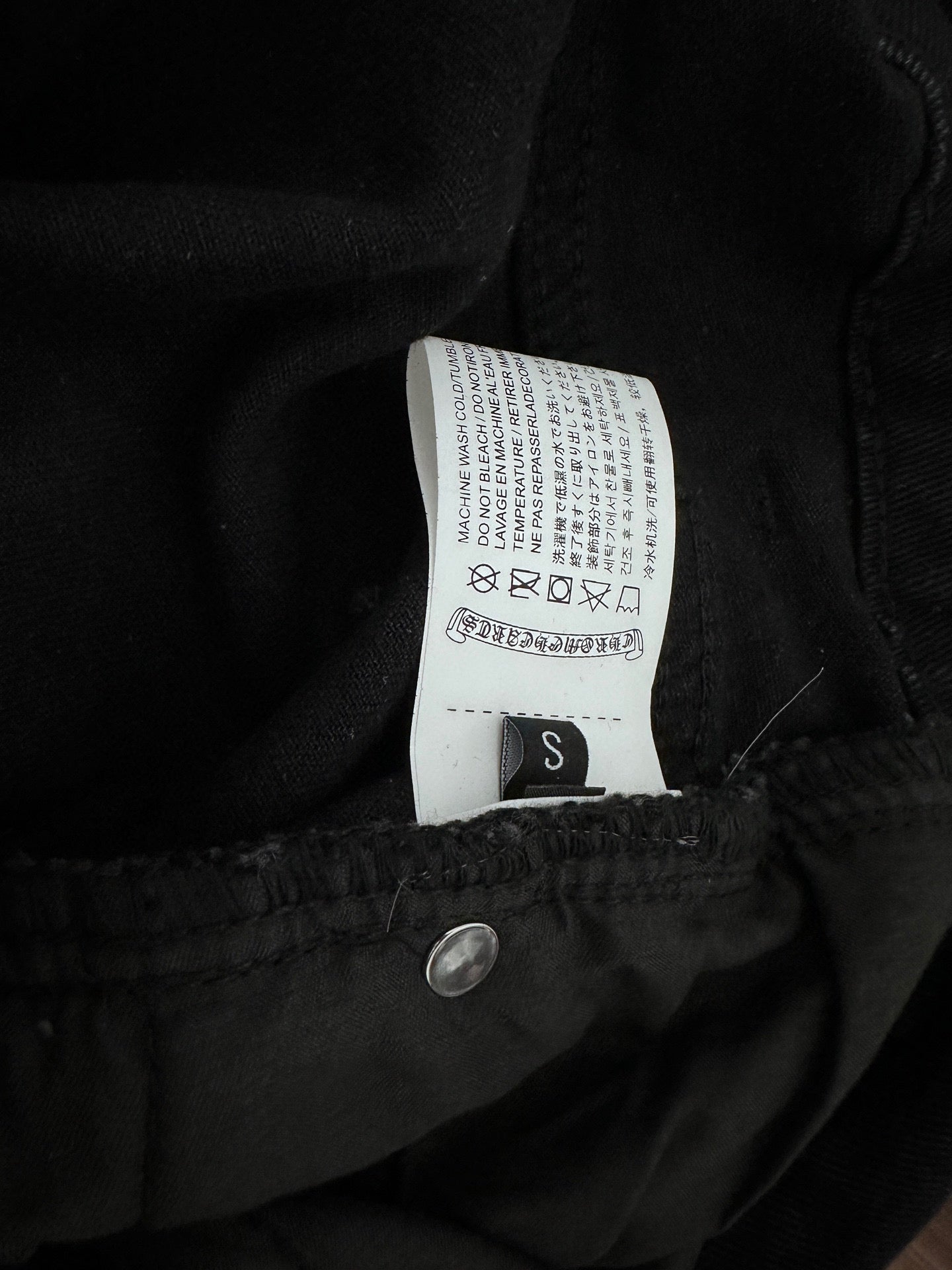 Dark denim pants inner waistband label with size S and care symbols