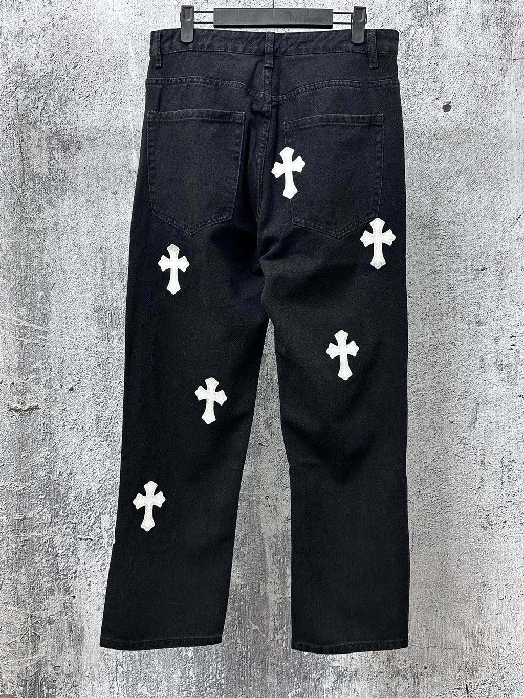 Dark denim pants with white cross applique patterns, side front view