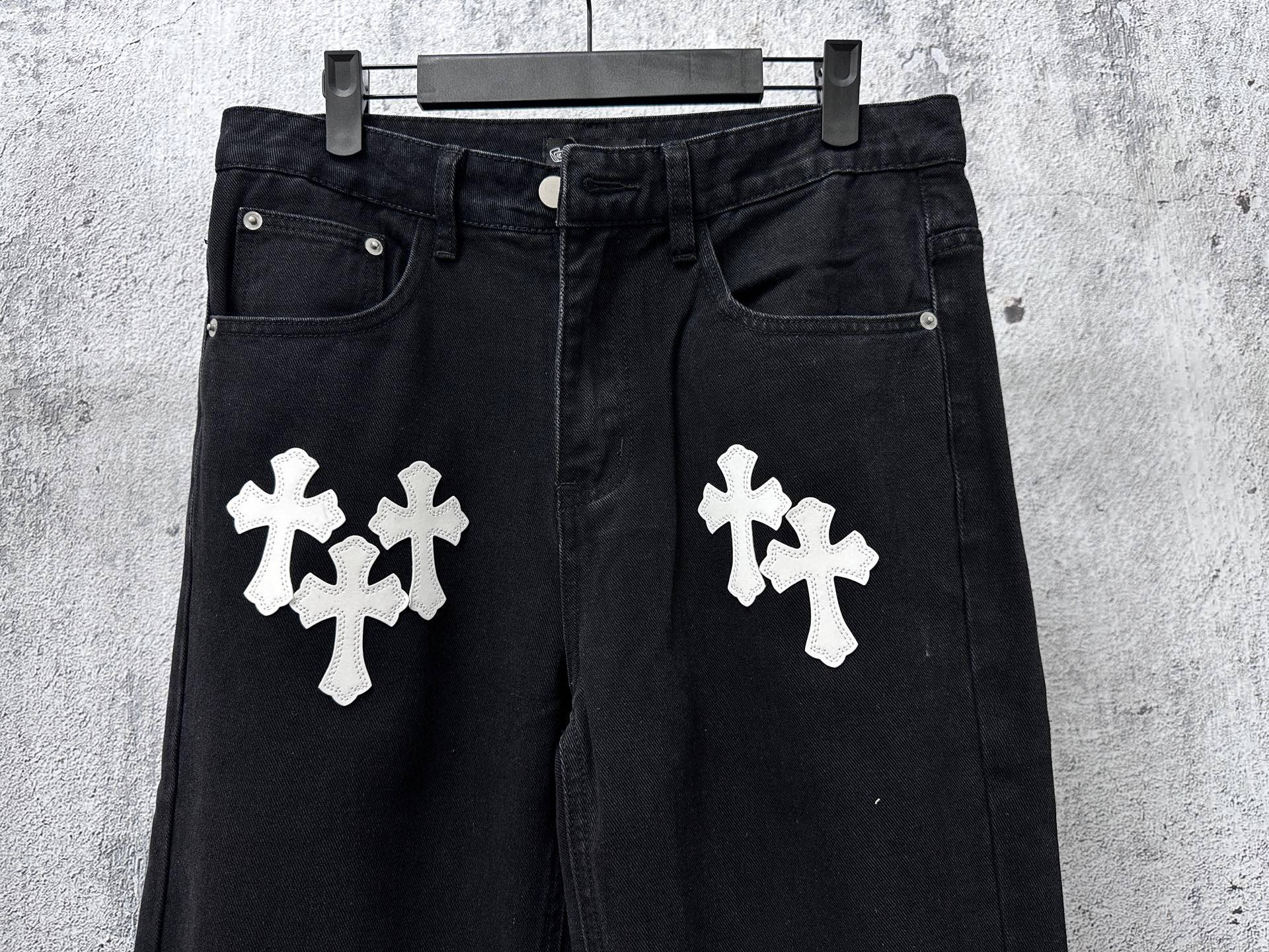 Dark denim pants with two white cross patches on front, button fly