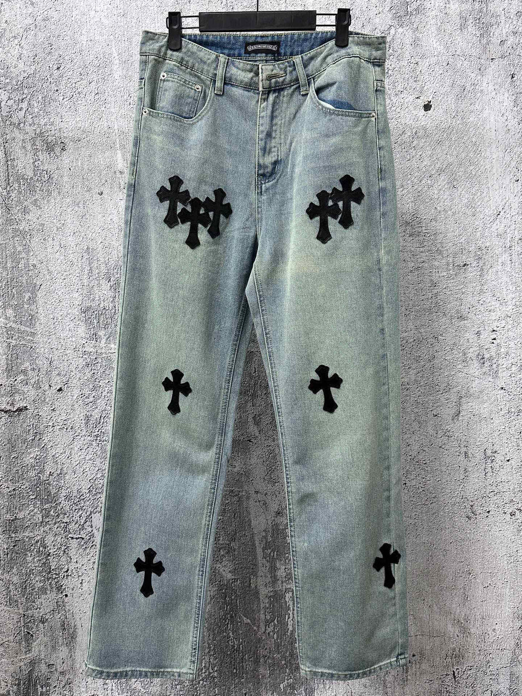 Light blue denim pants with black cross patches, button fly