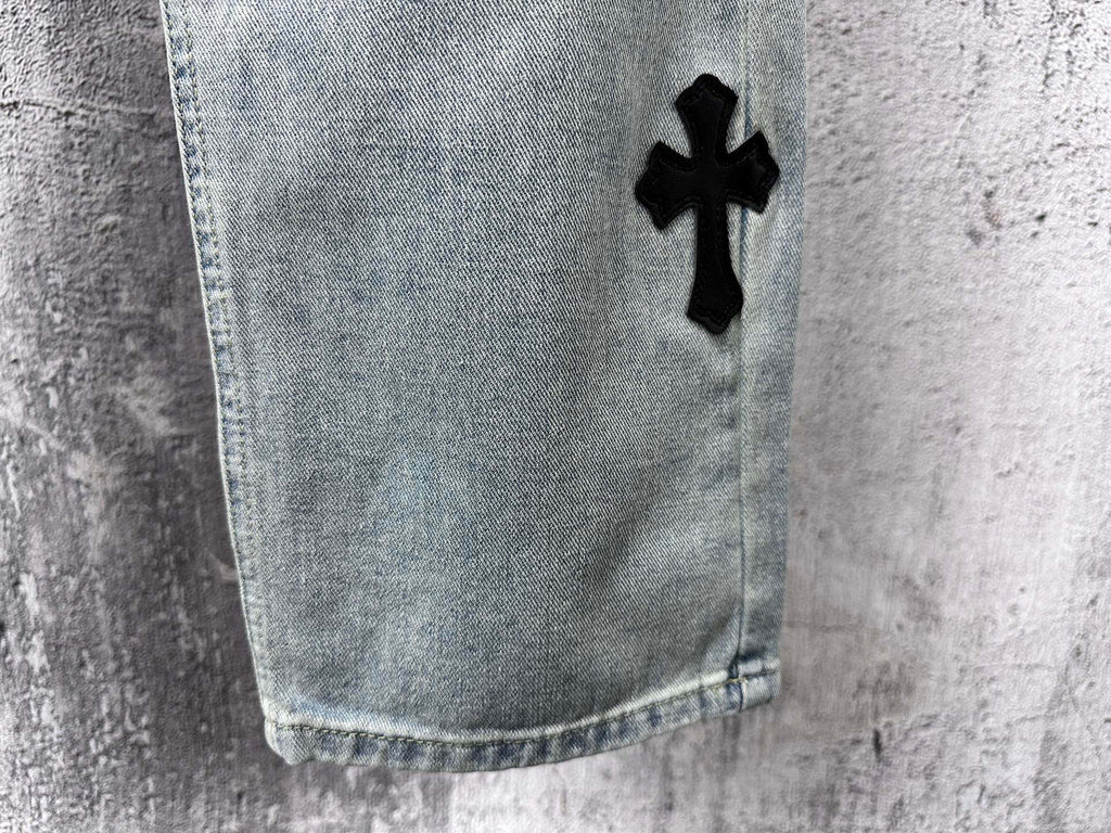 Light blue denim pants with black cross patch near hem