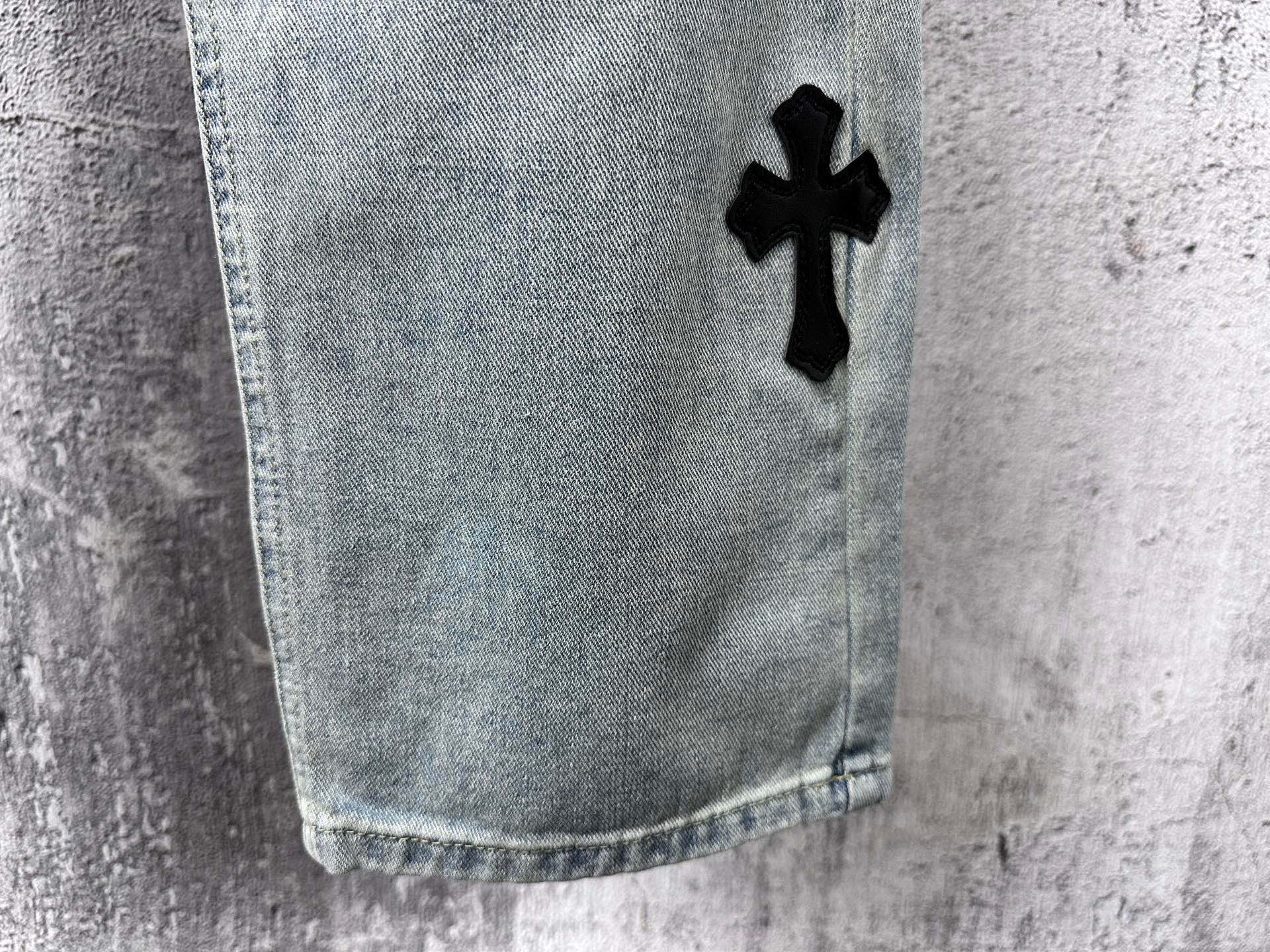 Light blue denim pants with black cross patch near hem