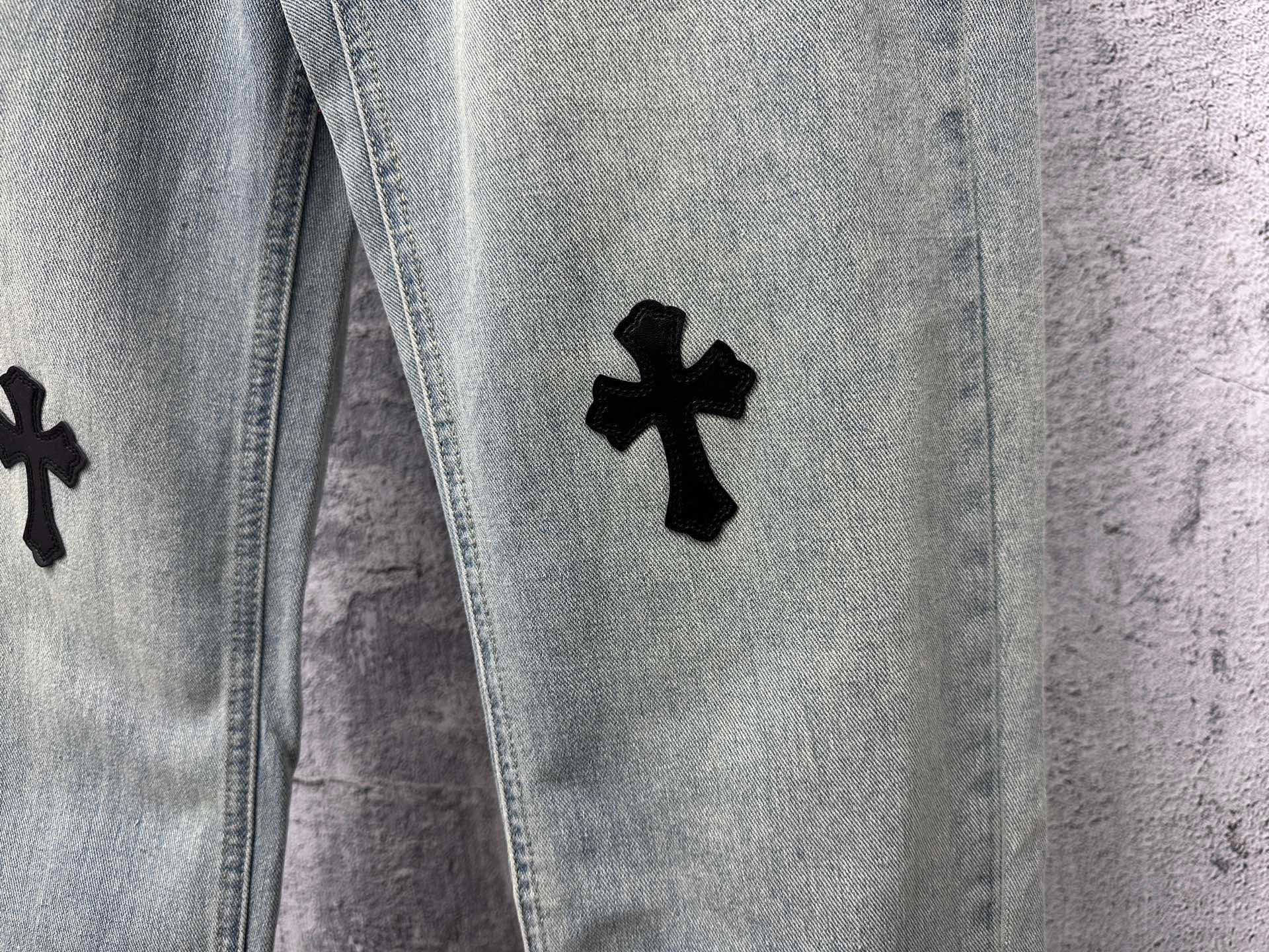 Light blue denim pants with a black cross patch on the leg