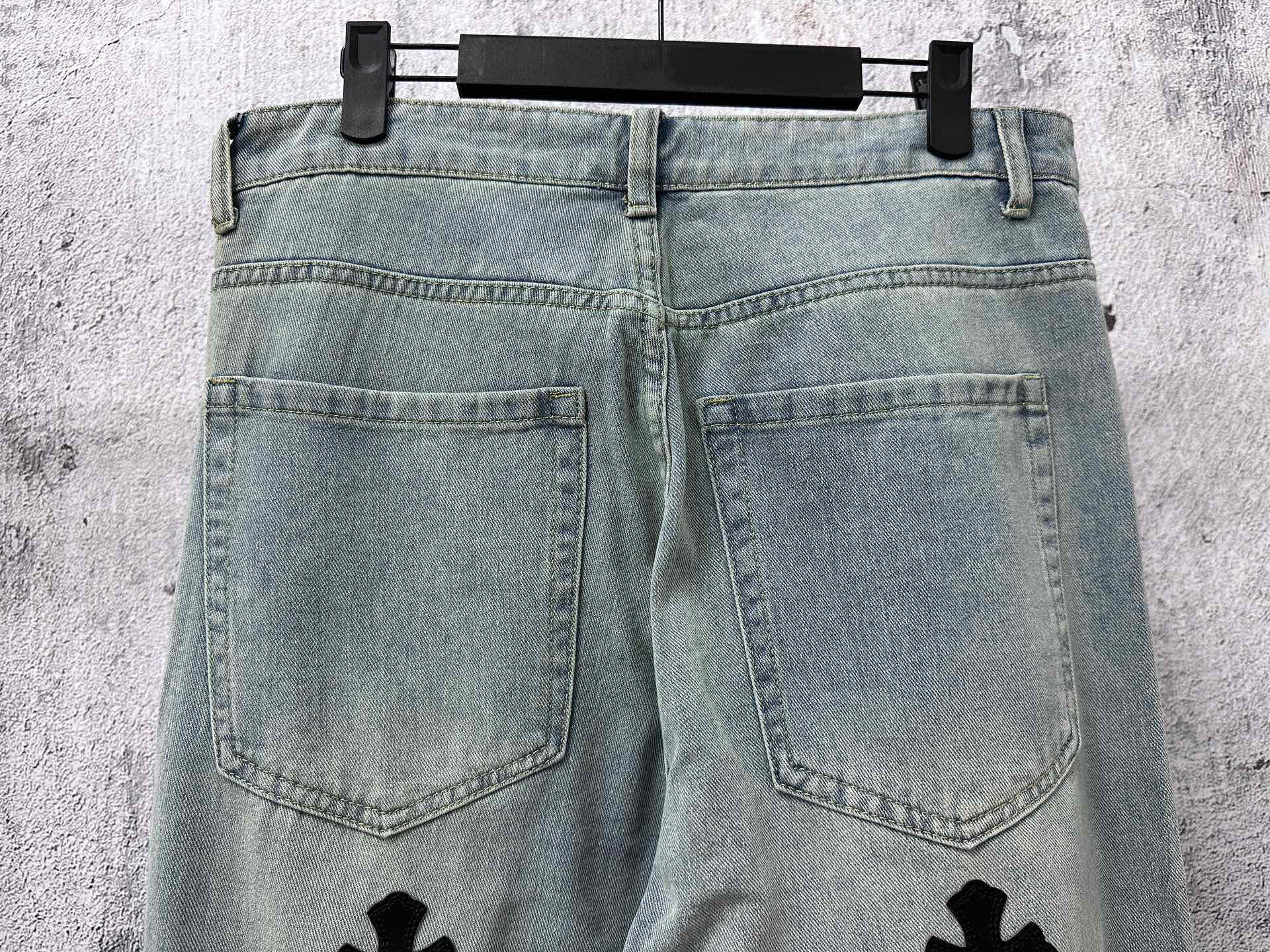 Light-wash denim pants with front pockets and small cross patches on legs