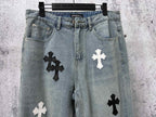 Light-wash denim pants with black and white cross patches near the thighs