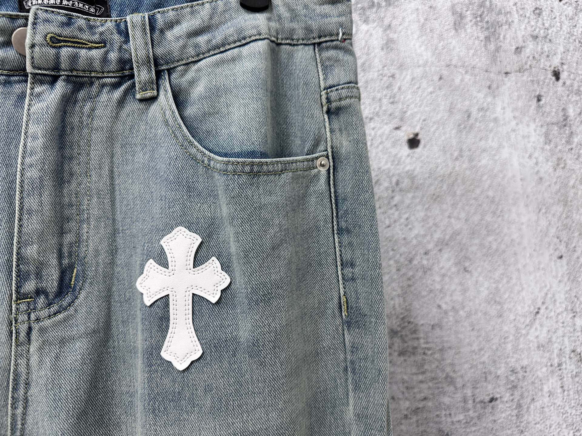 Light-wash denim waistband with belt loops and a large white cross patch