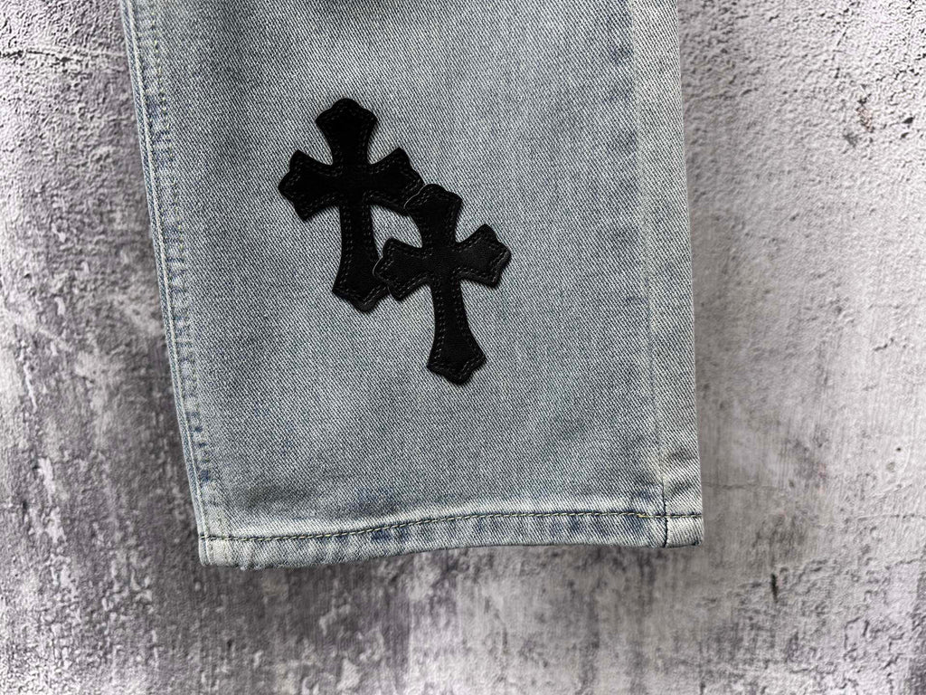 Light-wash denim cuff with a black cross patch on the leg