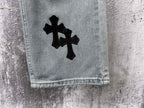 Light-wash denim cuff with a black cross patch on the leg
