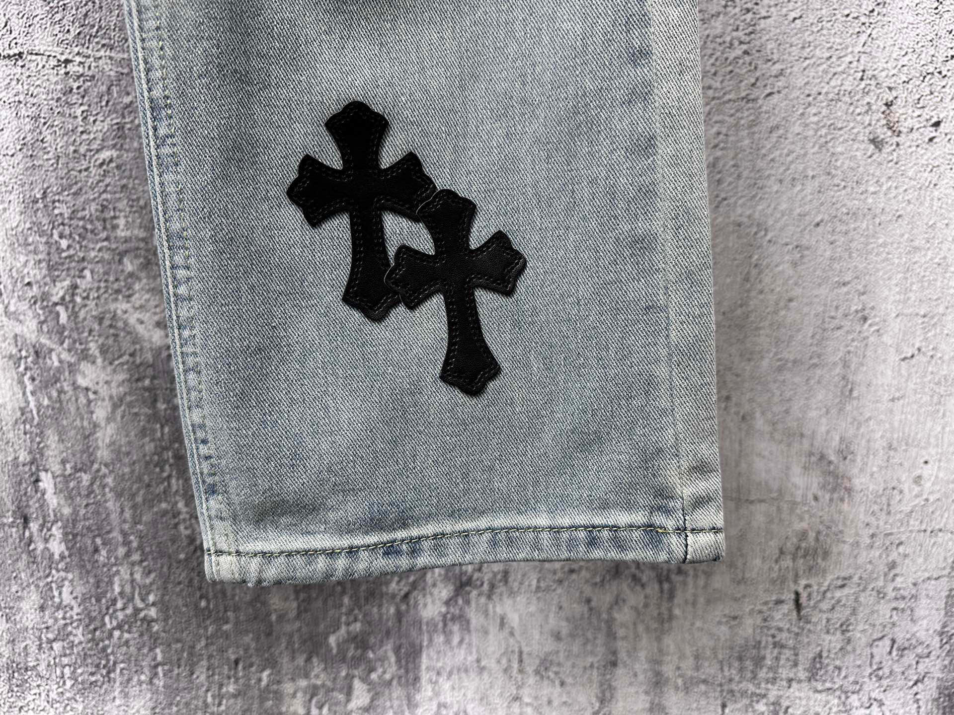 Light-wash denim cuff with a black cross patch on the leg