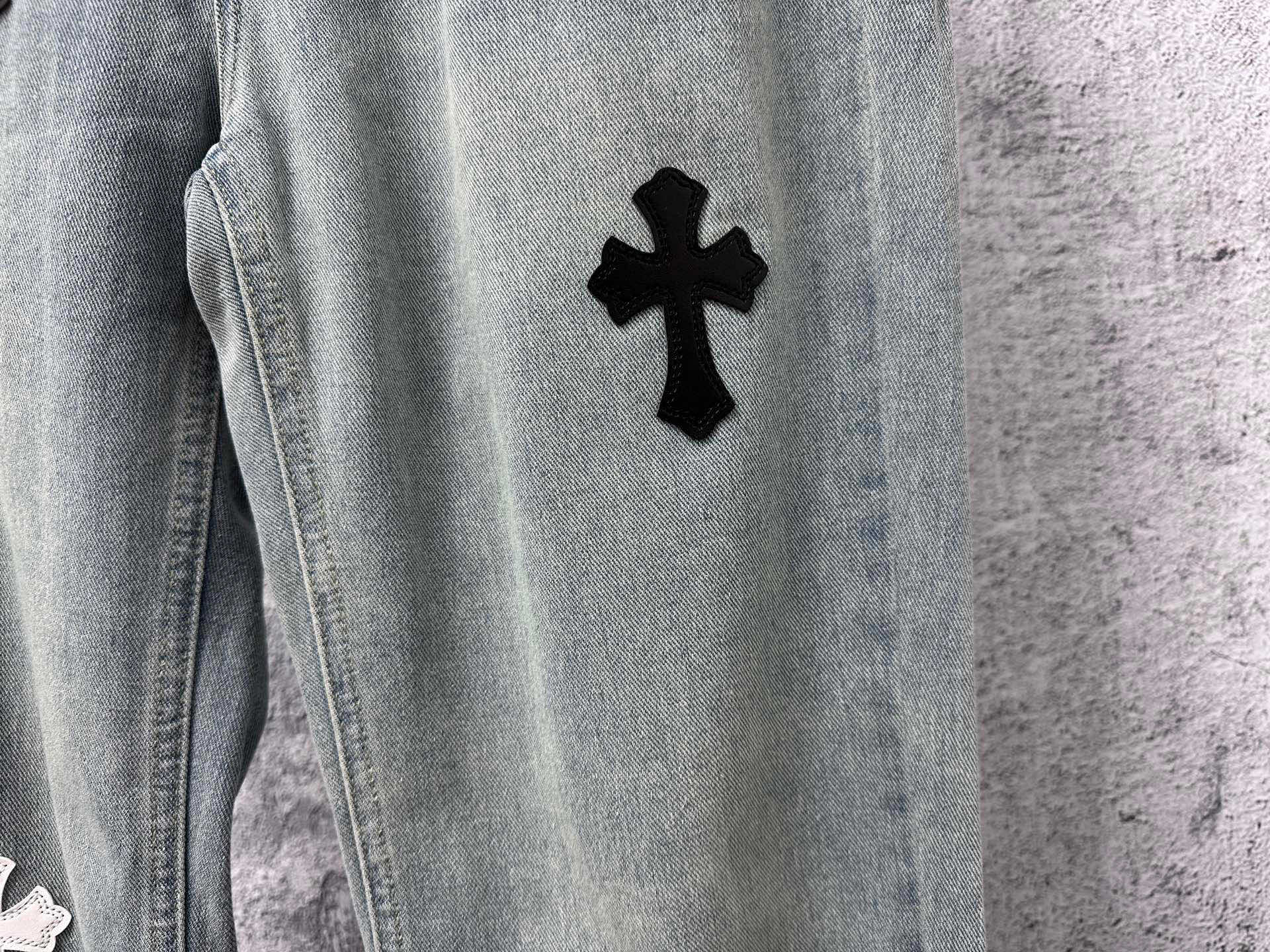 Light-wash denim leg with a black cross patch
